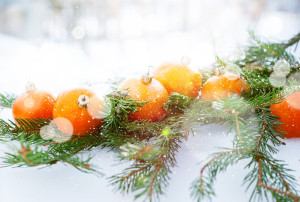 Greeting Card with Tangerines as Fir-tree Toy and Branch of Coniferous on White Snow, with boke and snowflakes